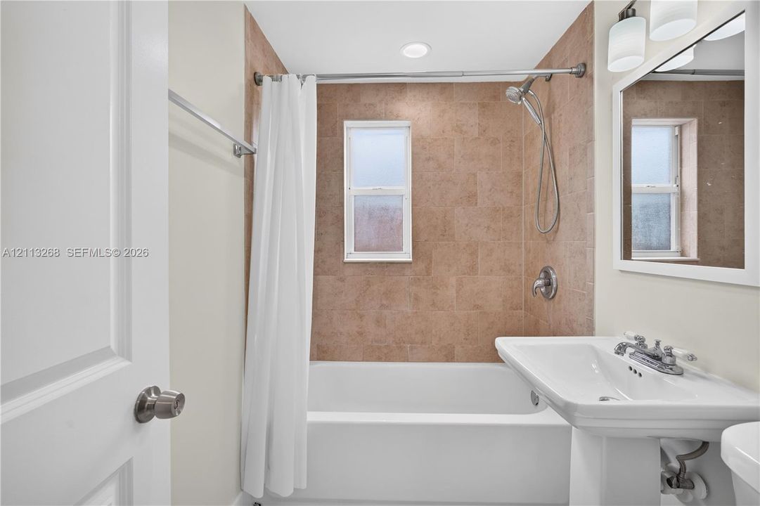 Bathroom featuring a pedestal sink, a bathtub with a tile surround, and a wall-mounted mirror with integrated light fixtures