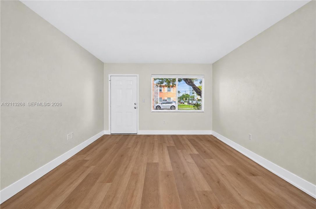 Interior space featuring wood-finish flooring, neutral wall tones, a six-panel entry door, and a single-pane window