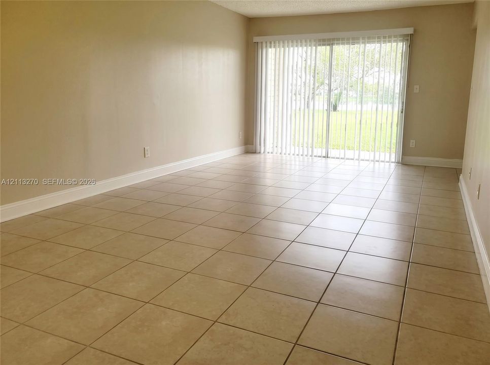 Spacious room featuring neutral tile flooring, smooth wall finishes, and glass sliding doors with vertical blinds