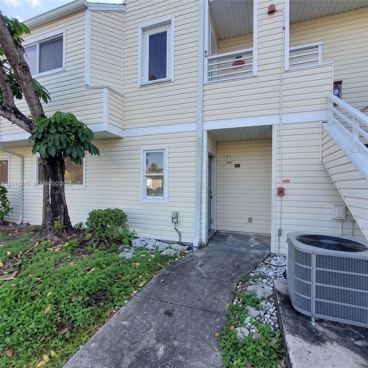 Multi-level exterior featuring light-toned horizontal siding, a private balcony with railing, an elevated staircase, and a concrete walkway