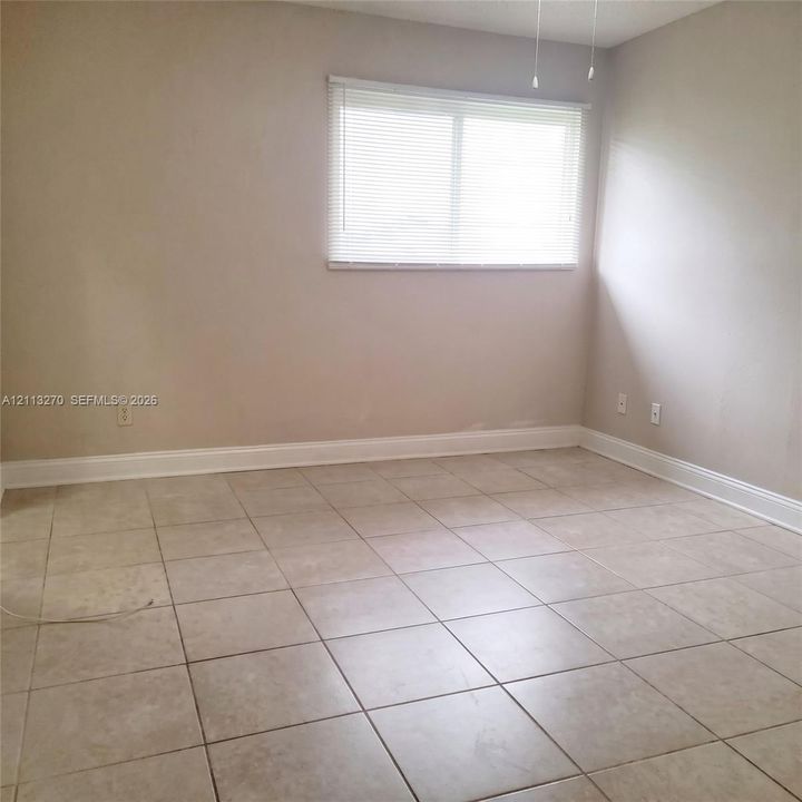 Neutral-toned room featuring large-format square tile flooring, a horizontal slider window, and an attached ceiling fan