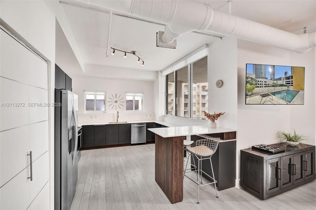 Modern kitchen featuring matte charcoal cabinetry, a built-in peninsula with a wood-finish base, stone-surface countertops, wood-finish flooring, and exposed ceiling ductwork