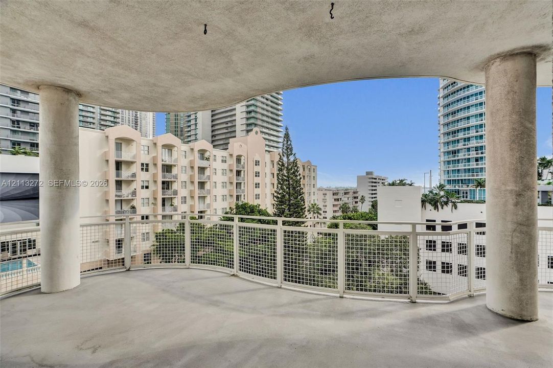 Covered balcony featuring concrete structural columns, a curved overhang, and a metal grid railing