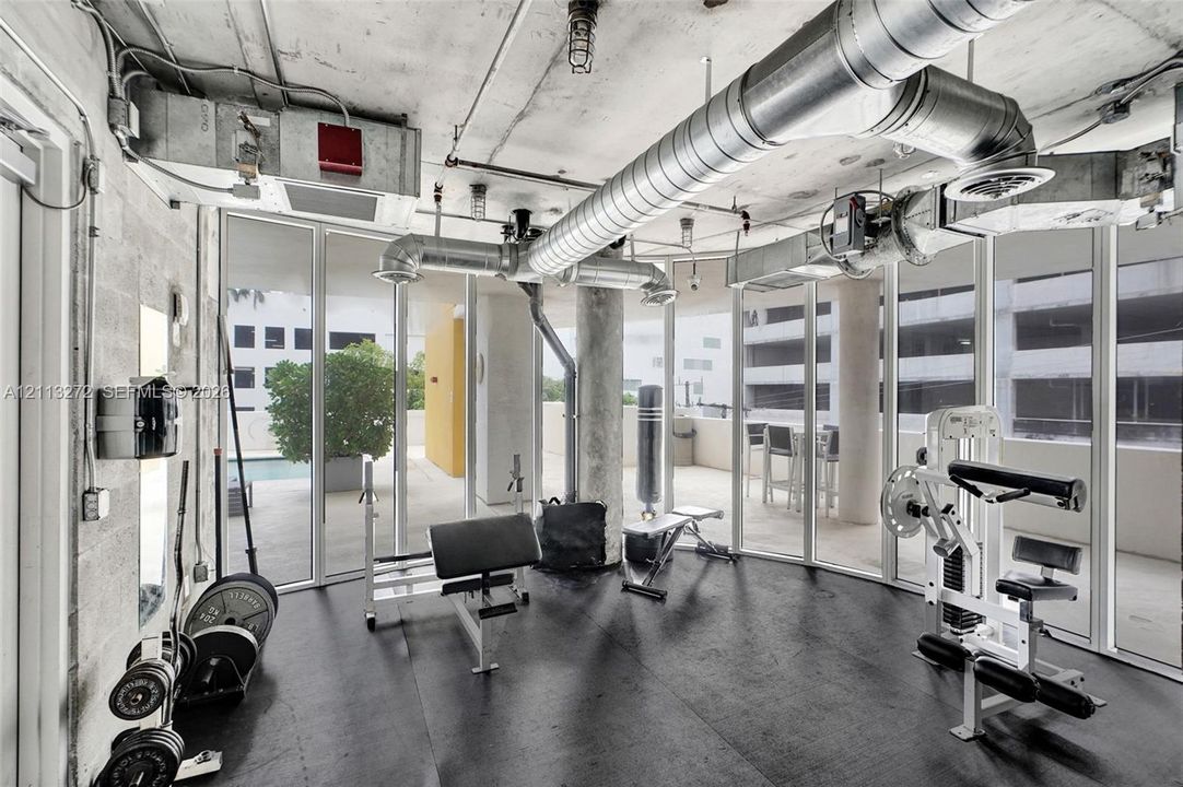 Industrial-style interior featuring exposed concrete ceilings, metallic ductwork, floor-to-ceiling glass wall panels, and impact-resistant rubber flooring