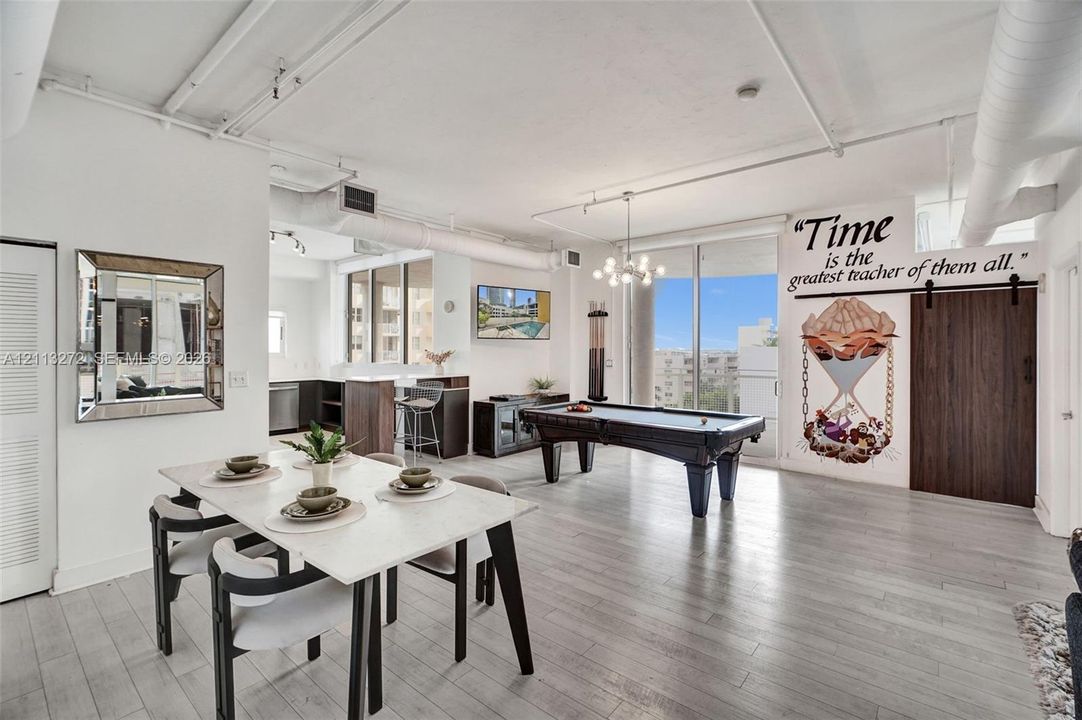 Open-concept interior featuring light wood-finish flooring, exposed industrial-style ceiling ductwork, floor-to-ceiling windows, and a dark wood barn-style sliding door