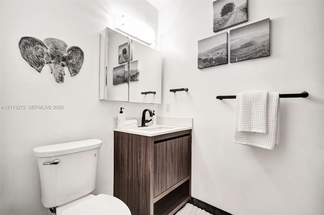 Wood-finish vanity with a stone-top sink, matte black faucet, mirrored medicine cabinet, and matte black towel hardware