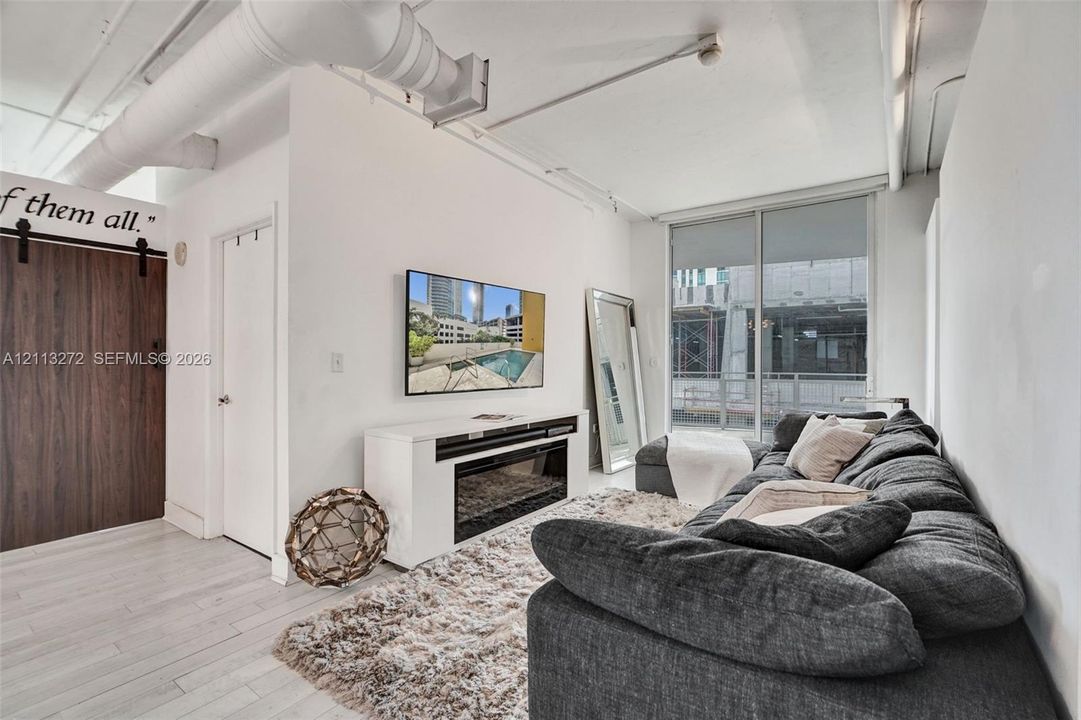 Industrial-style interior featuring exposed overhead ductwork, wood-finish sliding barn door, wood-finish flooring, and a glass sliding door providing exterior access