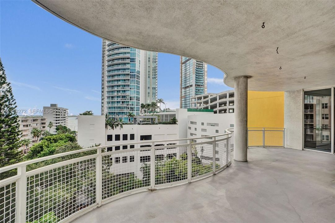 Covered balcony featuring a curved structural support column, concrete flooring, and metal grid railing