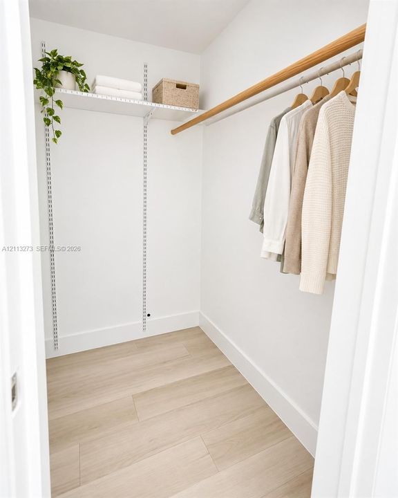 Storage space featuring adjustable metal shelving, a wall-mounted wood closet rod, and light-toned wood-finish flooring