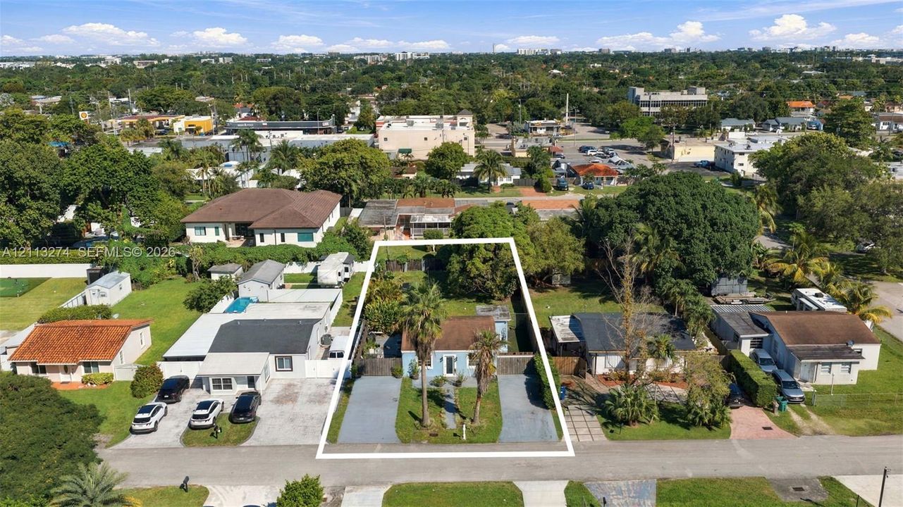 Aerial perspective of a detached property featuring dual paved driveways, established palms, and a fenced rear perimeter