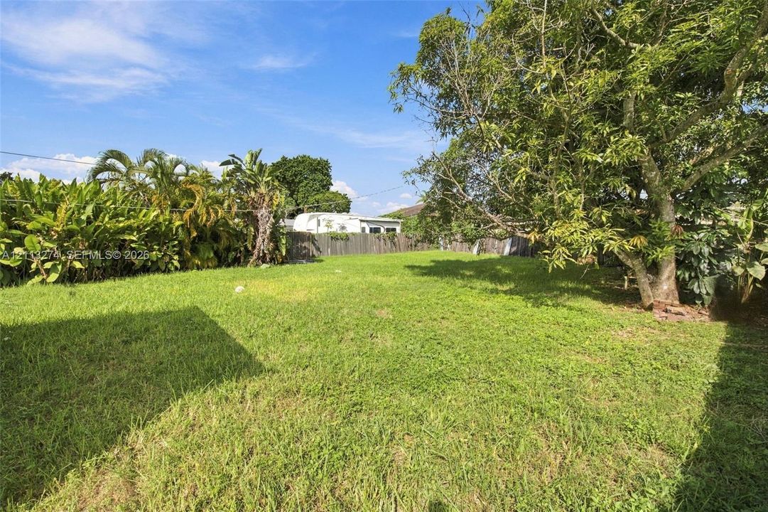 Expansive backyard featuring a lawn, perimeter wood fencing, and mature trees