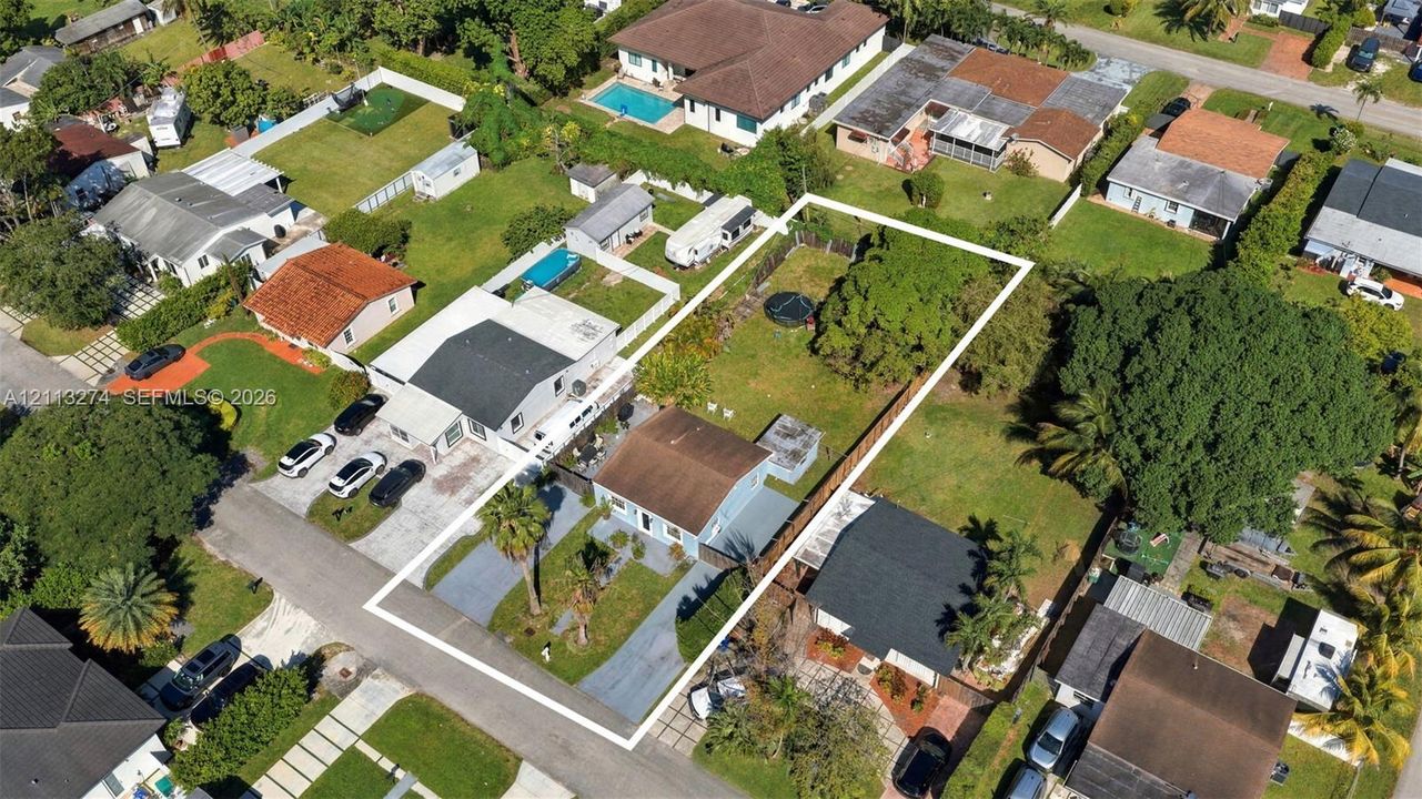 Aerial perspective of a property featuring an expansive rectangular lot, a paved driveway, and established mature trees