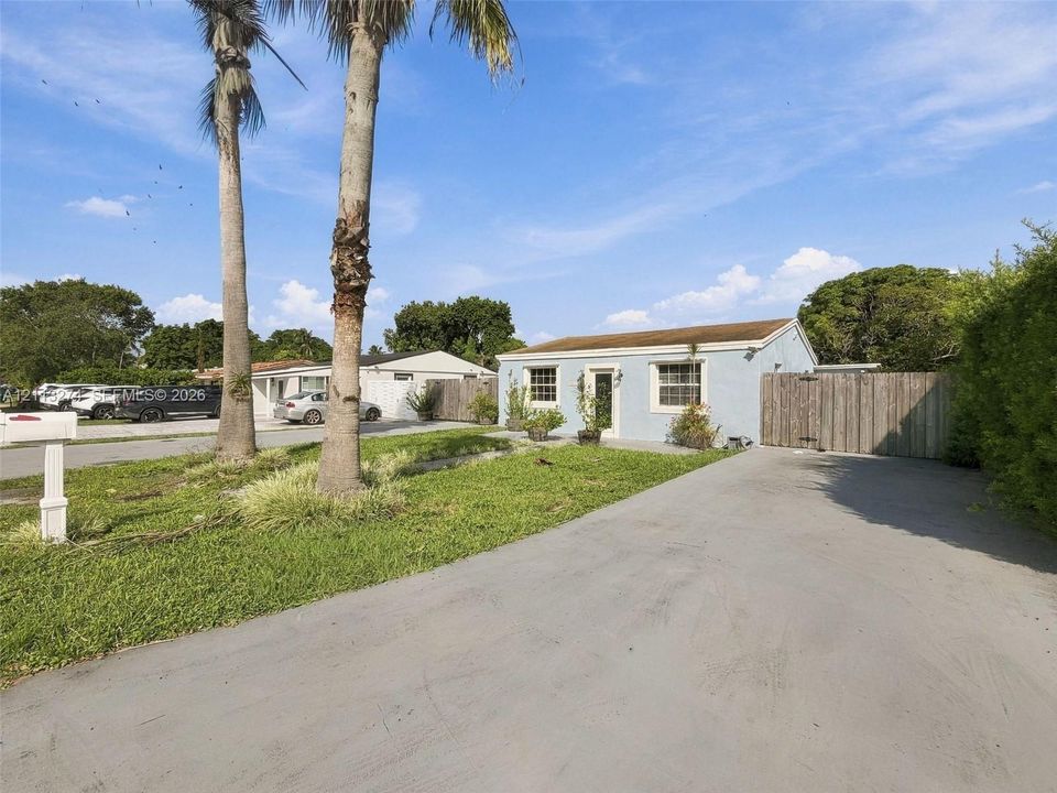 Exterior facade featuring light-toned stucco, multi-pane windows, paved driveway, and mature palm trees