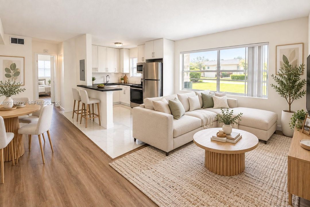 Open-concept interior featuring wood-finish flooring, white cabinetry, contrasting dark countertops, a breakfast bar, and a large picture window
