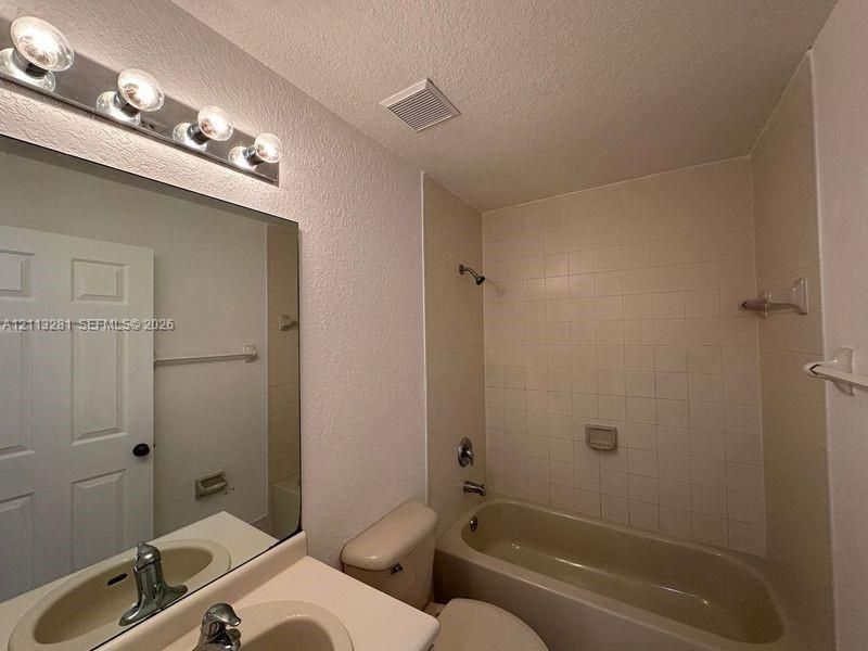 Bathroom featuring a vanity with integrated sink, large wall-mounted mirror, four-light vanity fixture, and a tiled tub-shower combination