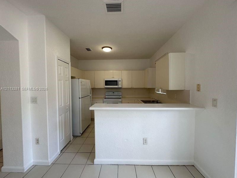 Kitchen featuring white cabinetry, solid-surface breakfast bar, tile flooring, and built-in appliances