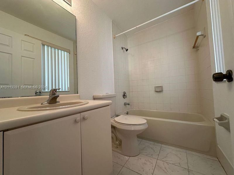 Bathroom featuring a vanity with an integrated sink, large wall-mounted mirror, ceramic tile flooring, and a tiled tub-shower combination