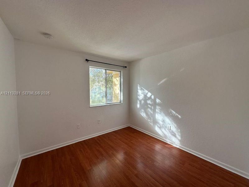 Room featuring wood-finish flooring, textured walls, and a single-pane sliding window with an integrated curtain rod