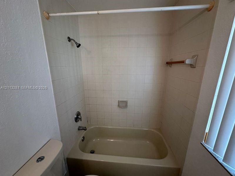 Full-height square wall tile surround, built-in soap dish, porcelain bathtub, chrome shower fixture, and wall-mounted towel bar