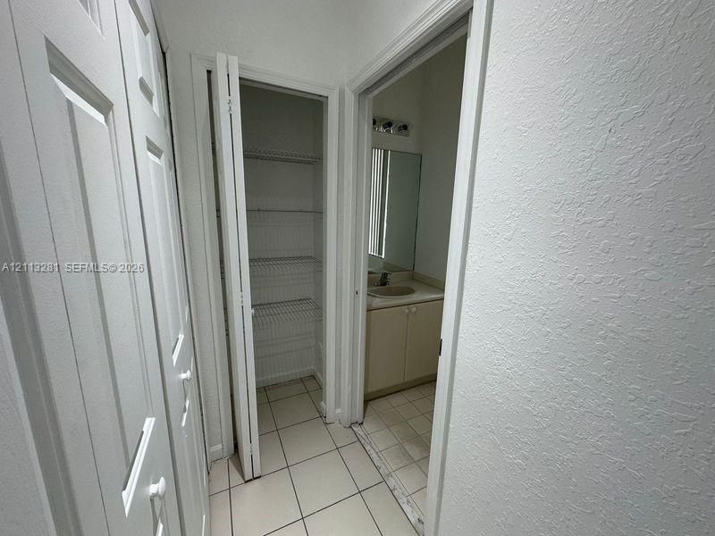 Storage area featuring floor-to-ceiling bi-fold doors, white wire shelving, tiled flooring, and a vanity with a neutral-toned countertop