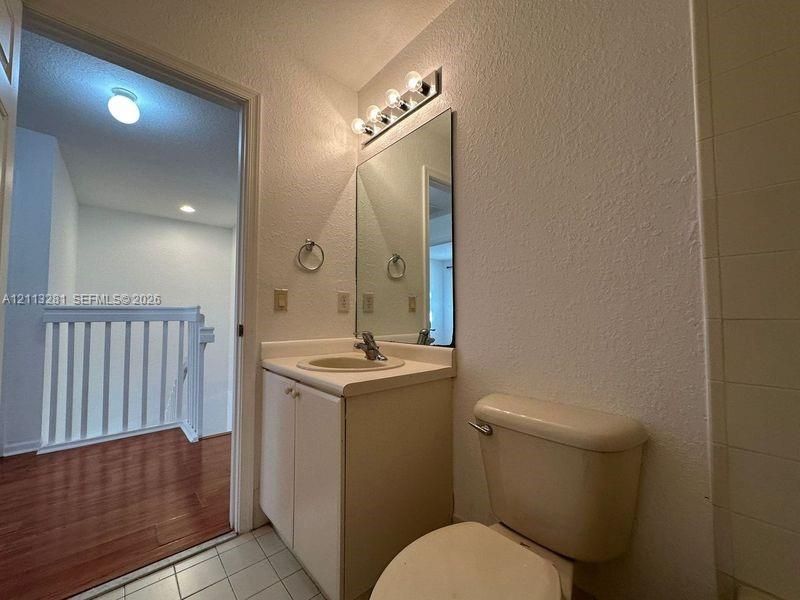 Bathroom featuring a vanity with an integrated sink, wall-mounted four-bulb lighting fixture, rectangular mirror, and tile flooring