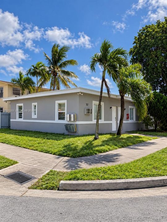 Single-story exterior featuring a neutral painted finish, crisp white trim, and established palm trees situated on a corner lot