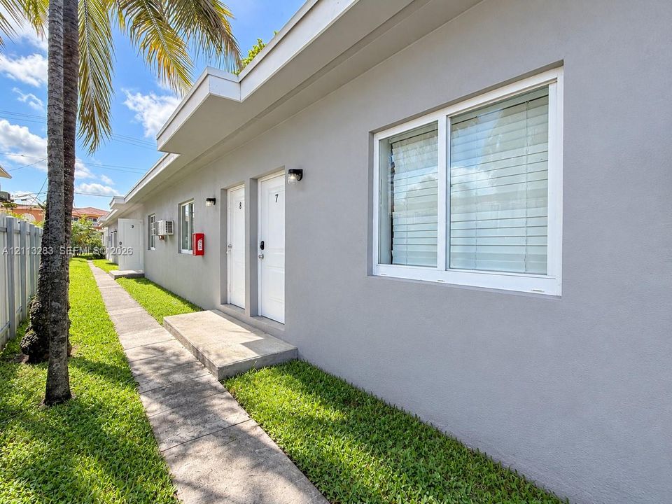 Exterior featuring smooth gray stucco facade, white-trimmed dual-pane windows, concrete walkways, and manicured lawn