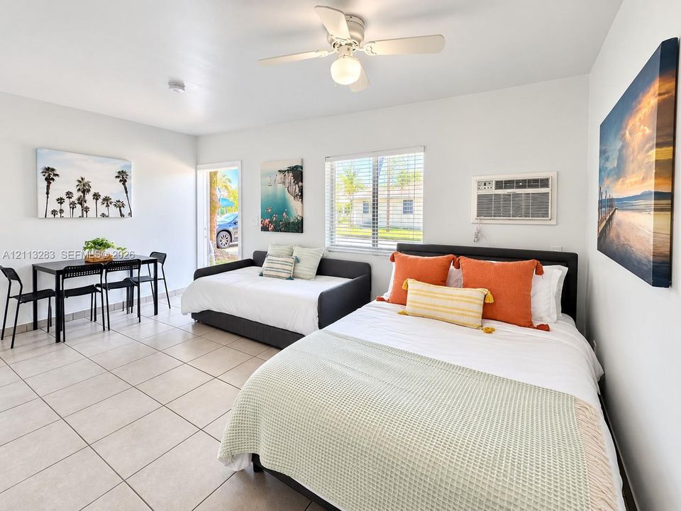 Large-format neutral tile flooring, ceiling fan with integrated lighting, and wall-mounted air conditioning unit