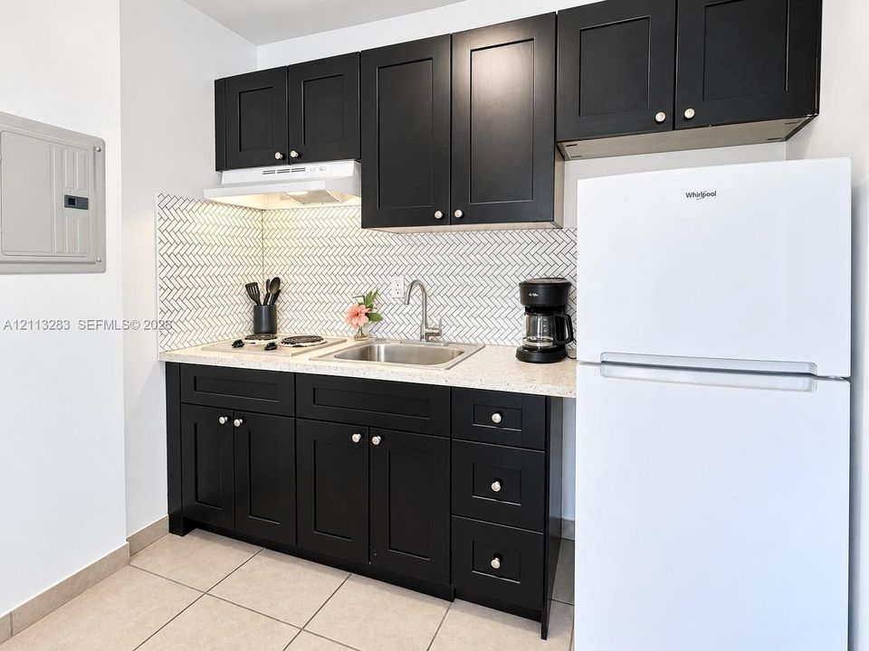Kitchen featuring matte black shaker-style cabinetry, white herringbone patterned backsplash, stone-finish countertop, stainless steel sink with high-arc faucet, and integrated stovetop