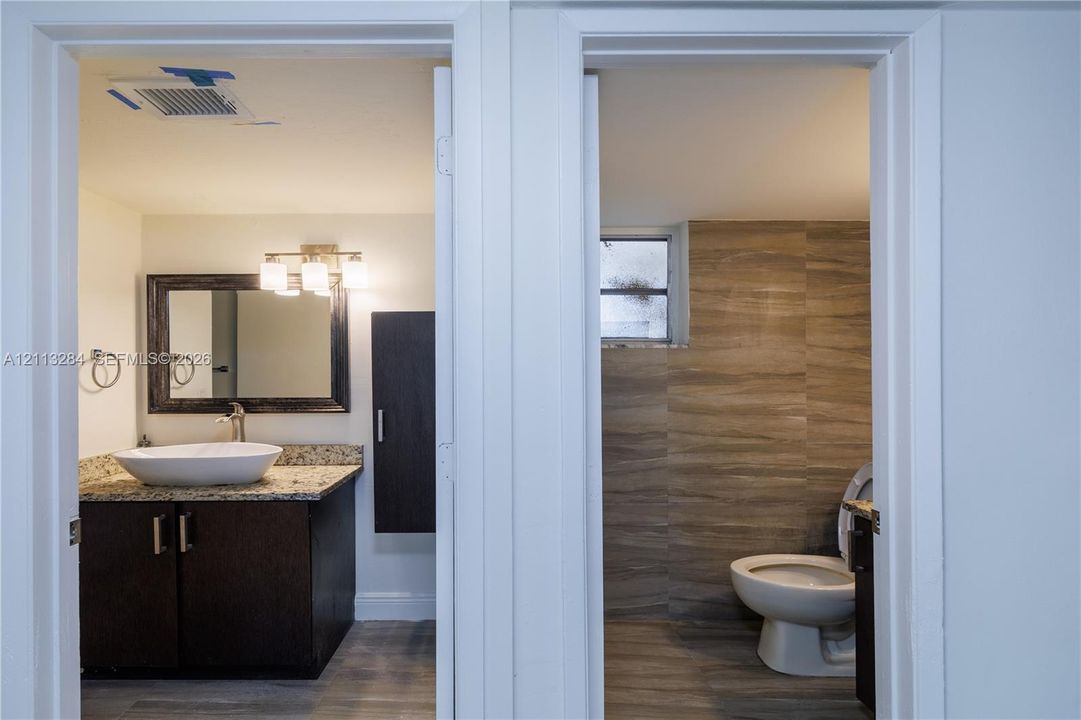 Bathroom featuring a dark wood-finish vanity with a stone countertop, a white vessel sink, a framed mirror, and tile-accented walls