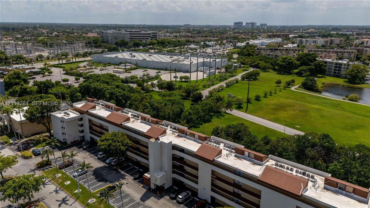 Multi-story residential building featuring a low-slope roof, stucco facade, integrated covered parking, and proximity to expansive green space with mature landscaping
