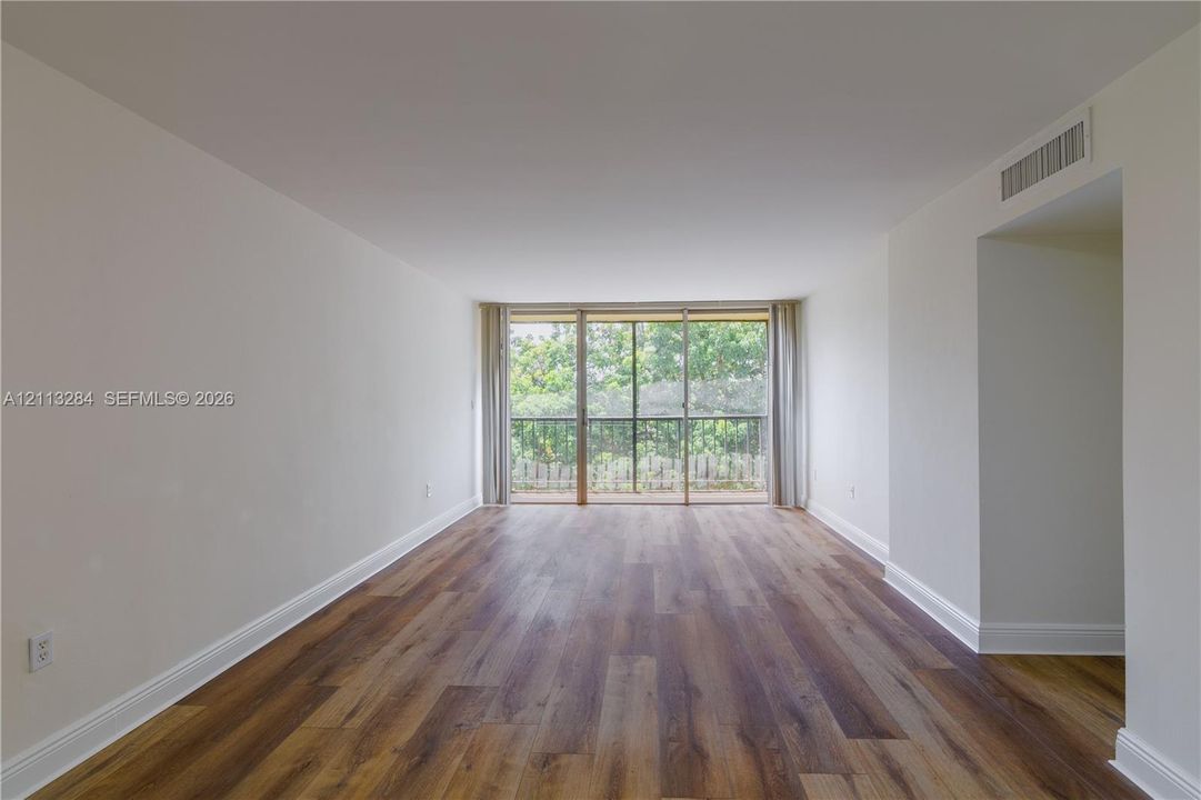 Living space featuring wood-finish flooring, neutral walls, and a large sliding glass door opening to an exterior balcony