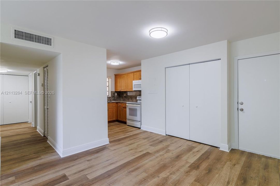 Wood-finish flooring throughout, kitchen featuring wood cabinetry, white appliances, dual-door closet storage, and flush-mount ceiling lighting