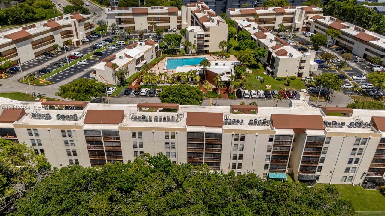 Multi-story residential complex featuring low-slope roofing, designated surface parking, and a central swimming pool with surrounding hardscaping