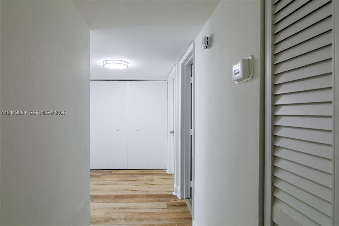 Hallway featuring wood-finish flooring, dual-door built-in closet, louvered closet door, and a flush-mount circular ceiling light