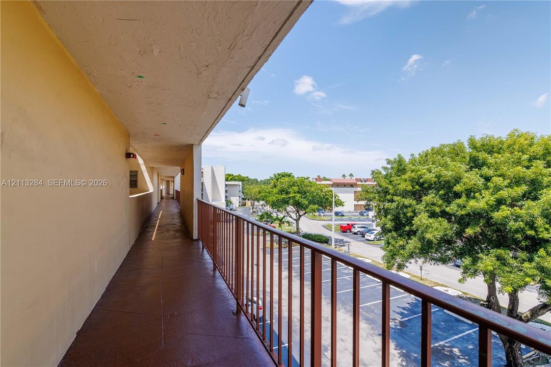 Exterior walkway featuring a covered roofline, painted concrete flooring, and a metal railing