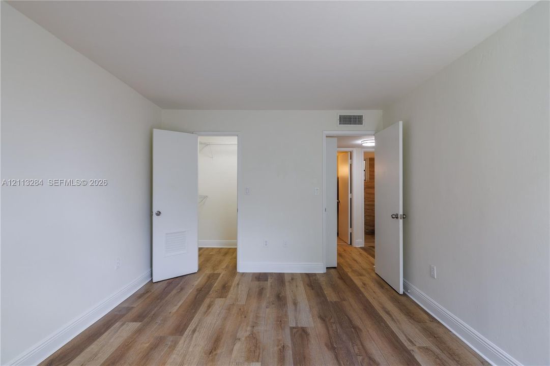 Interior room featuring neutral wall paint and wood-finish flooring, accompanied by a walk-in closet with built-in wire shelving