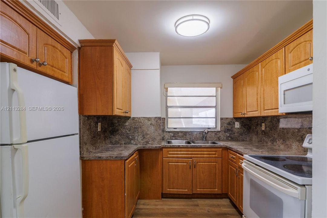 Kitchen featuring wood-finish cabinetry, stone-patterned laminate countertops, double-basin stainless steel sink, wood-finish flooring, and white built-in appliances