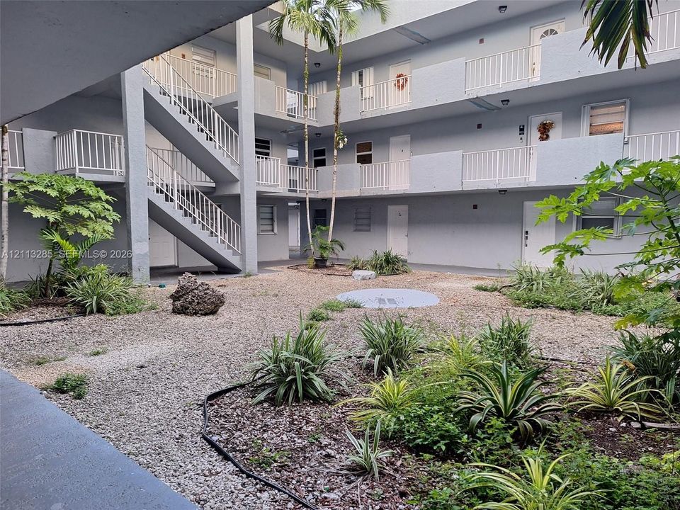 Multi-level structure featuring a gravel courtyard, palm trees, white metal railings, and exterior staircases