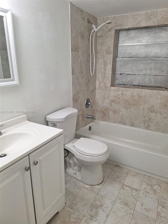 Bathroom featuring a white vanity cabinet with an integrated sink, stone-finish floor tiling, stone-finish tub surround, and a jalousie window