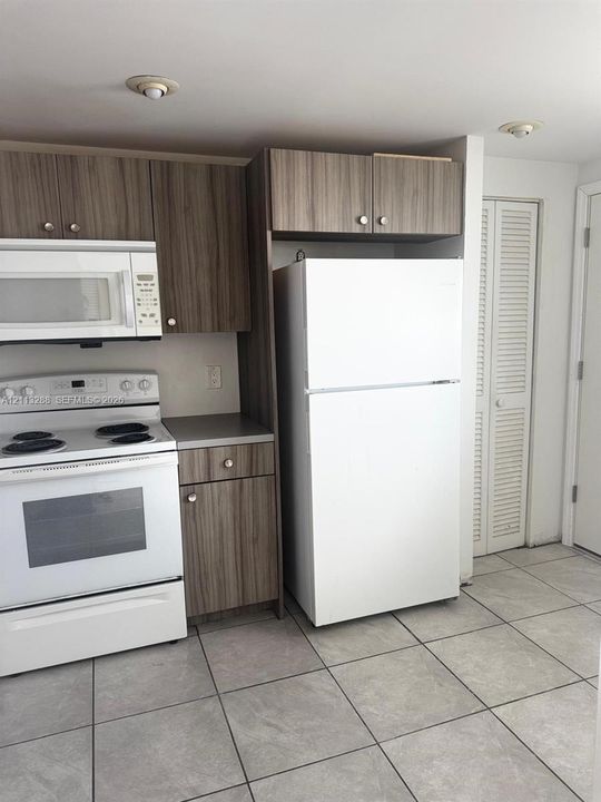 Kitchen featuring wood-finish cabinetry, white appliances, and large-format tile flooring with louvered closet doors