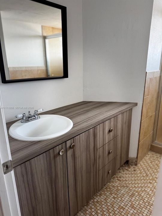 Vanity featuring wood-finish cabinetry, a drop-in sink, dual-handle chrome faucet, wall-mounted mirror with a black frame, and tiled flooring