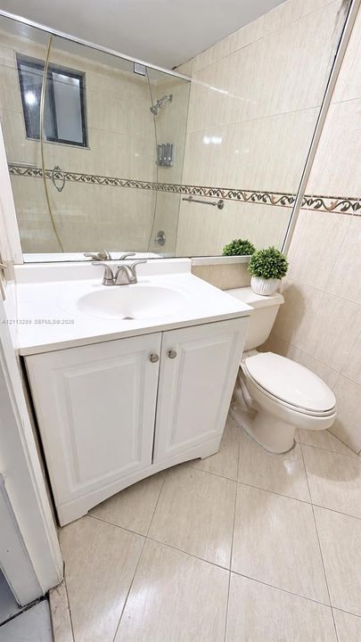 Bathroom featuring a white vanity cabinet, integrated sink, large wall-mounted mirror, and tile flooring
