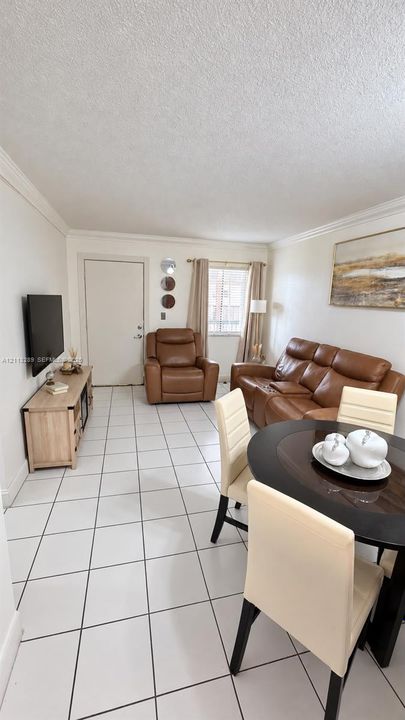 Living area featuring white ceramic tile flooring, crown molding, and natural light from a single-pane window