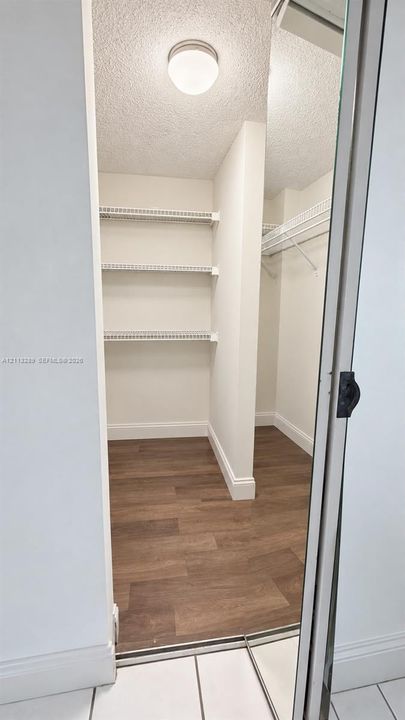 Walk-in closet featuring wood-finish flooring, white built-in wire shelving, and a mirrored sliding door