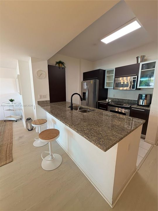 Kitchen featuring a peninsula with stone-finish countertops, stainless steel appliances, dark cabinetry, and a high-arc matte black faucet