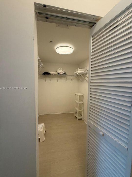 Storage closet featuring white louvered doors, neutral wood-finish flooring, and built-in wire shelving