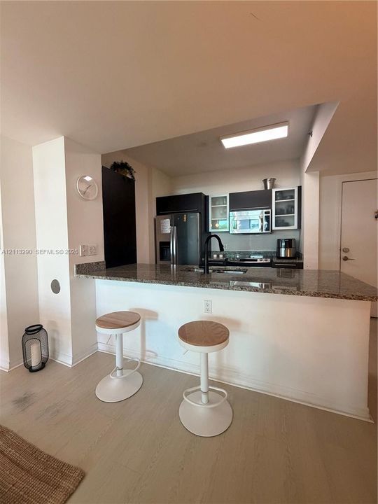 Kitchen featuring a stone-surface breakfast bar, dark cabinetry, stainless steel appliances, a gooseneck faucet, and light-tone wood-finish flooring
