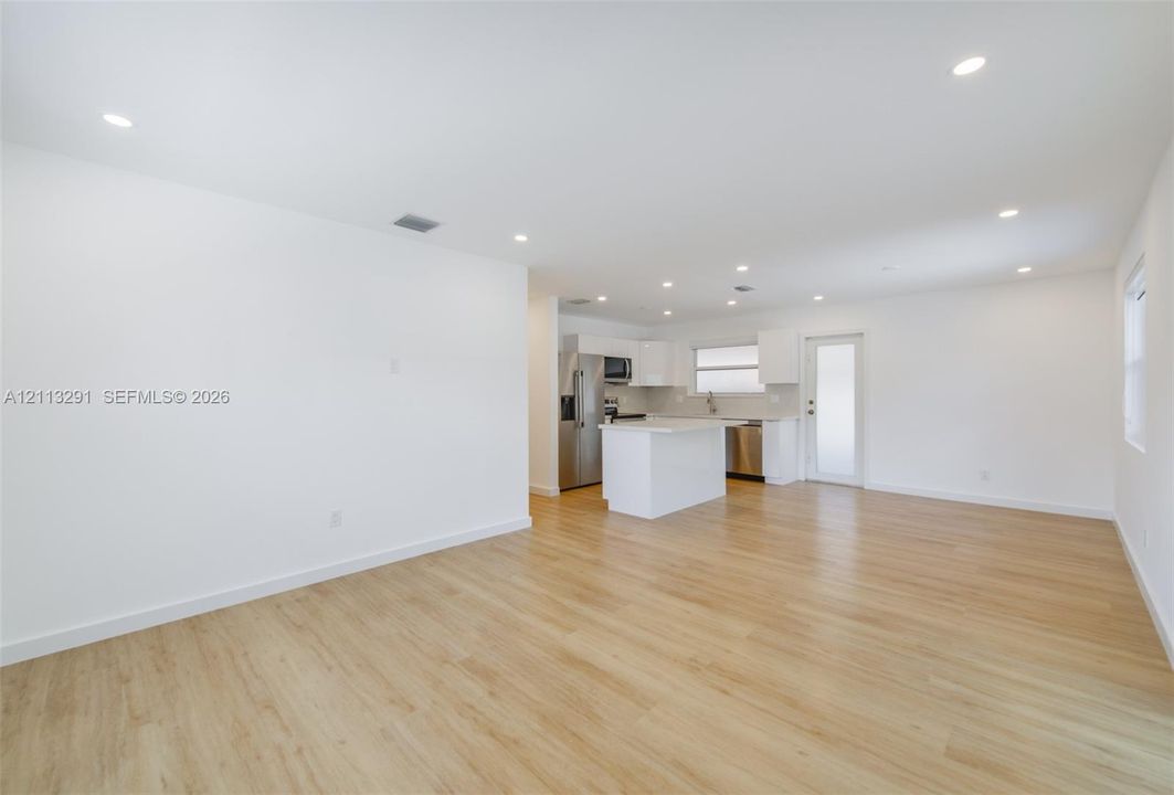 Open floor plan featuring wood-finish flooring, recessed lighting, white cabinetry, a center island, and stainless steel appliances