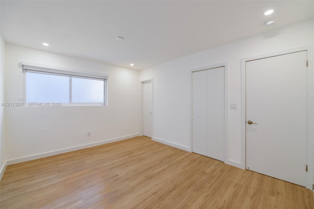 Neutral-toned interior featuring wood-finish flooring, recessed lighting, a horizontal sliding window, and solid-core doors